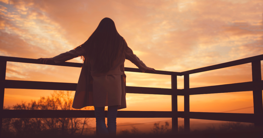 夕暮れにそっと考えながら夕焼けを見る女性