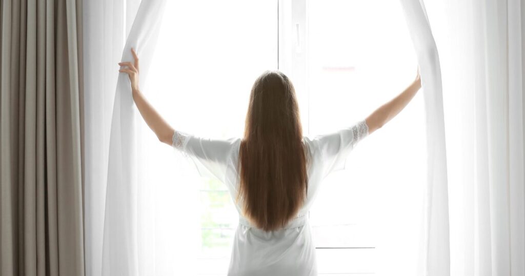 カーテンを開ける前向きな女性