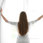 カーテンを開ける前向きな女性