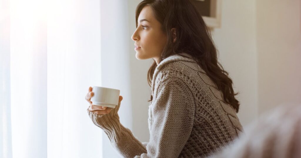 窓辺でコーヒーを持つ女性