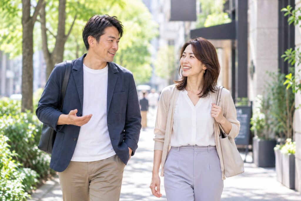 40代男女が横並びで歩いている場面。恋人っぽく手をつながせず、少し距離があり、話しながら自然に笑っている。
